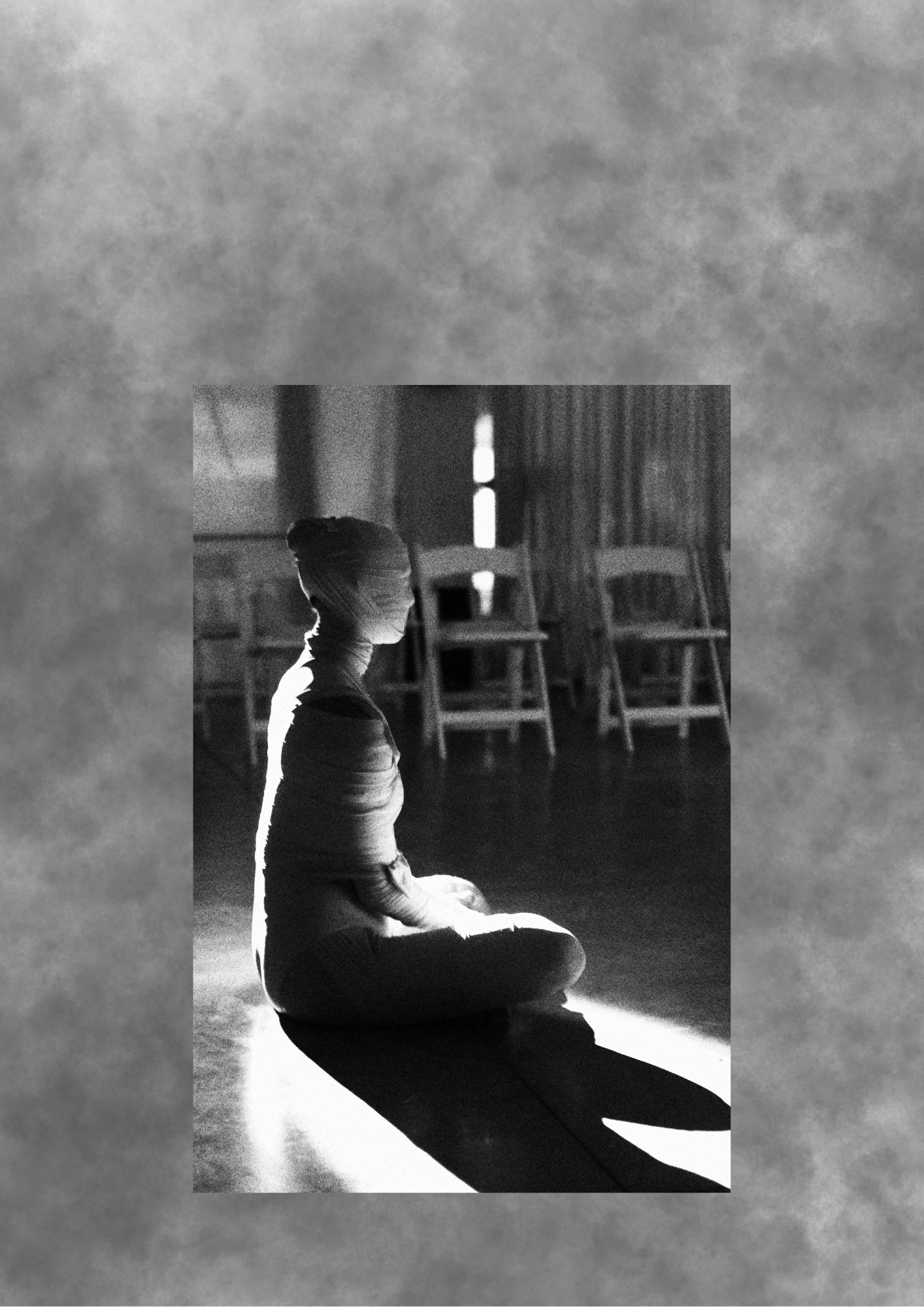 Wrapped seated figure illuminated by a beam of light.